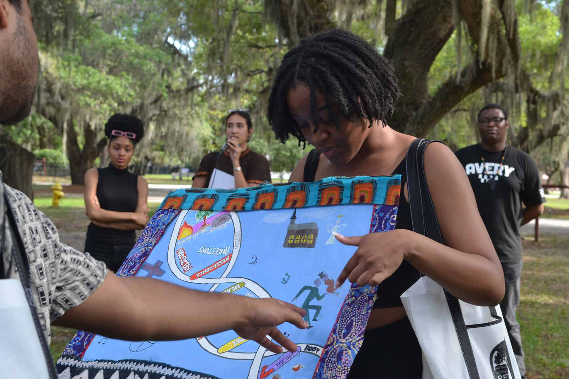 A group of people stand outdoors as a woman points to details on a colorful quilt or fabric artwork, featured in the 2025 Willson Center Annual Report, held by another person.